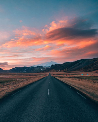 Empty road leading towards mountains against cloudy sky during sunset