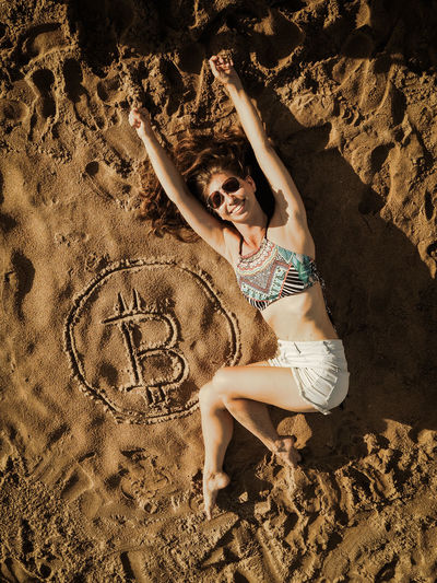 Full length of woman lying by bitcoin symbol at beach