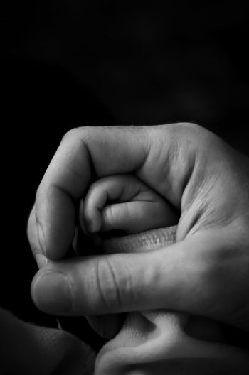Cropped image of father holding son hand against black background