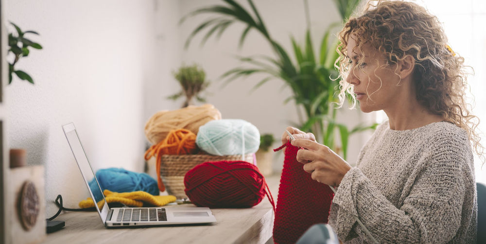 Woman knitting while looking at laptop