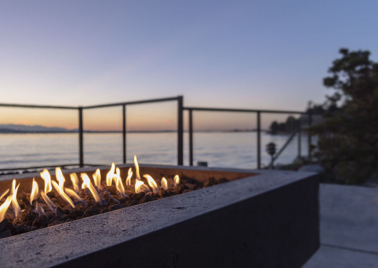 Backyard gas lit fire pit at golden hour blue hour sunset by the waters edge. copy space, no people.