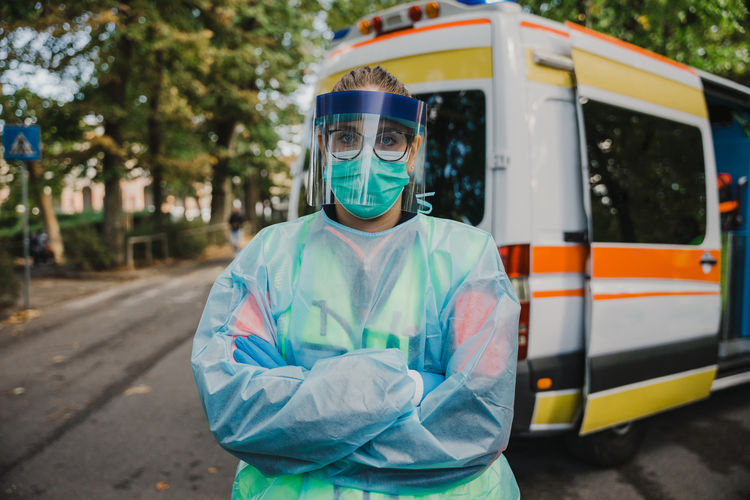 Portrait of doctor wearing protective suit standing against ambulance
