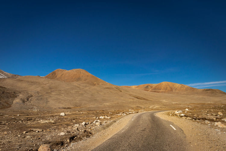 Scenic view of dirt road against clear blue sky