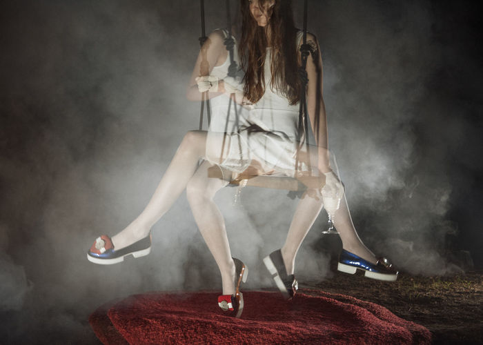 Double exposure image of young woman sitting on swing