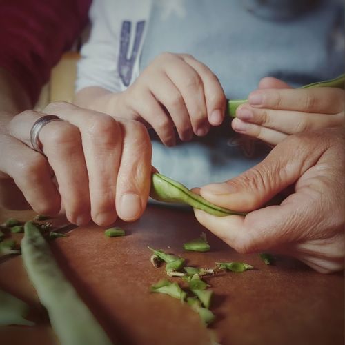 Cropped hands of woman with child cleaning green beans at table