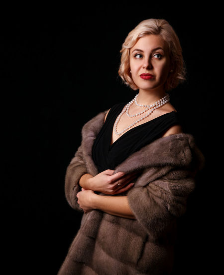 Portrait of young woman standing against black background