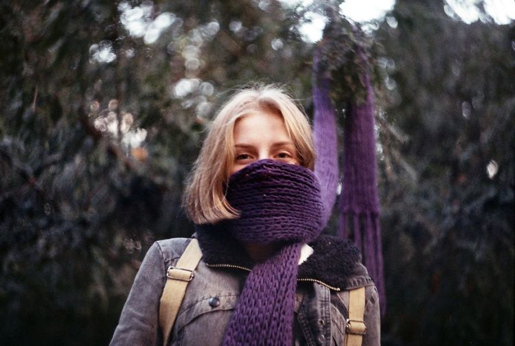 Low angle portrait of woman wearing purple woolen scarf against trees