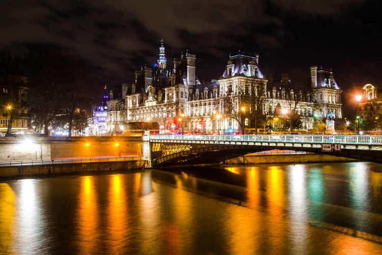 Illuminated bridge over river against sky in city at night