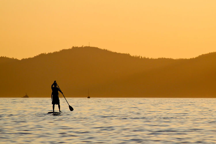 Rear view of man paddleboarding at lake against sky during sunset