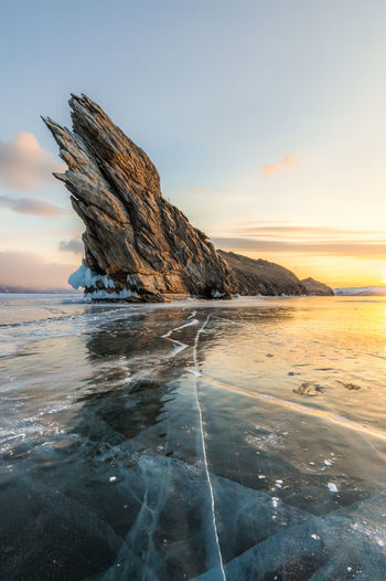 Scenic view of rock formation in frozen sea against sky at sunset