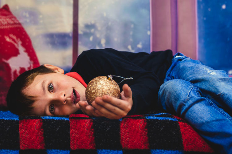 Caucasian blond boy lying down holding a christmas toy looking at camera. merry christmas
