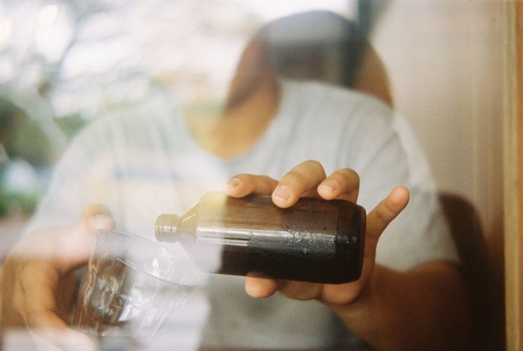 Midsection of man pouring cold brew in glass seen from window