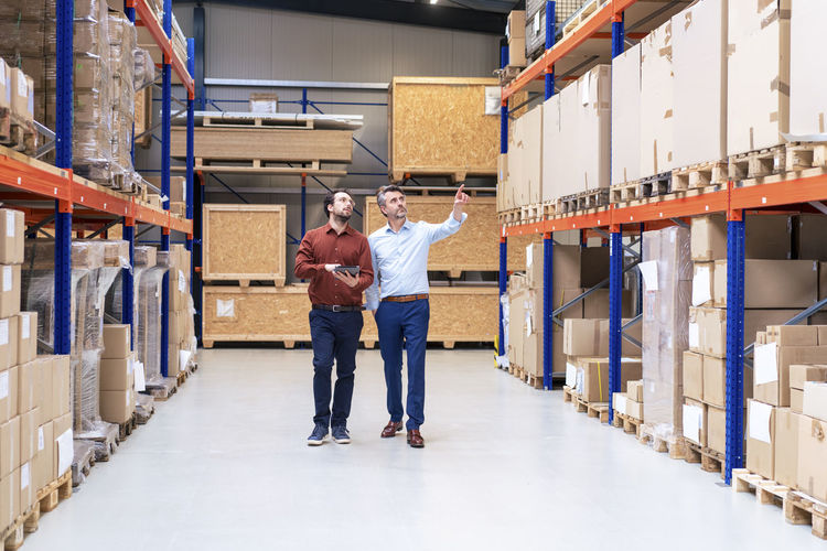 Businessman with colleague pointing at containers in warehouse
