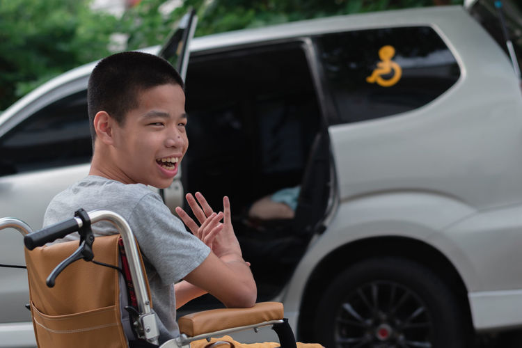 Portrait of smiling boy on wheelchair against car
