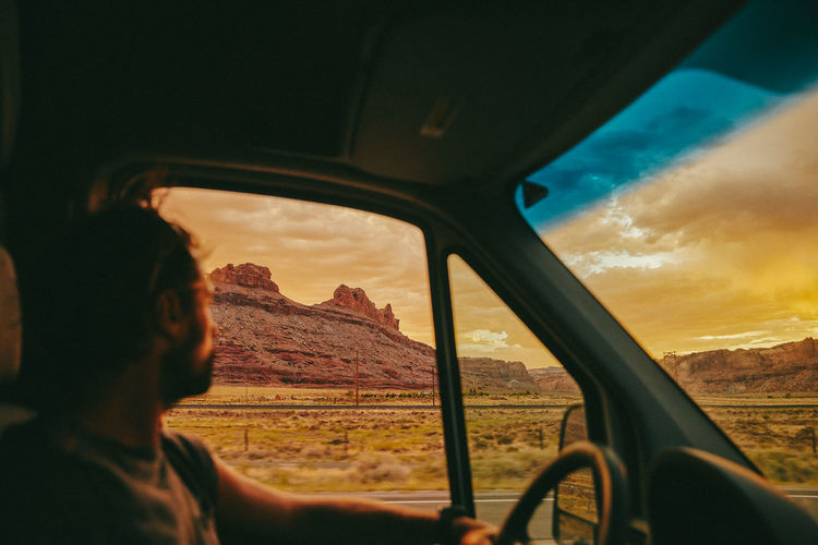 Young man gazing out to sunset while driving in desert of moab, utah.