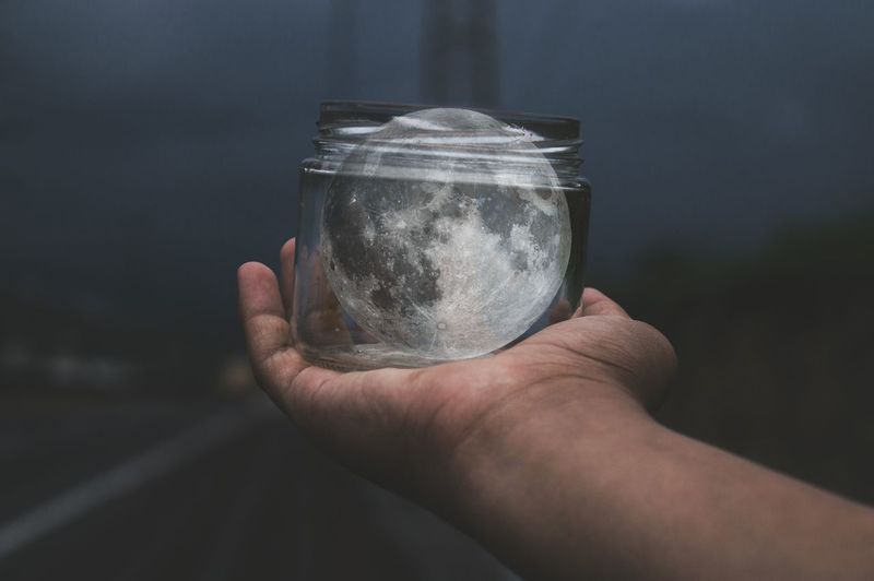 Cropped hand of man holding moon in jar at night