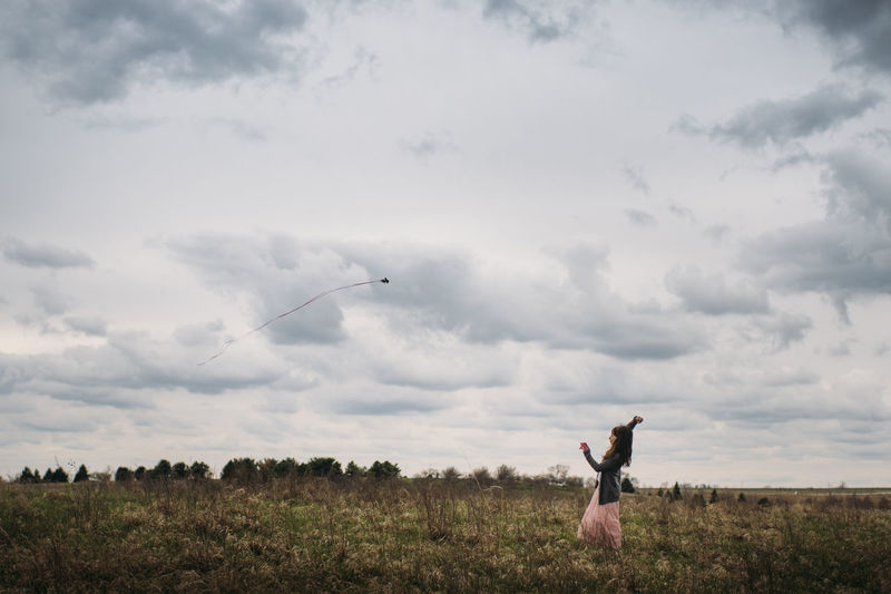 Side view of playful girl flying kite against cloudy sky at park