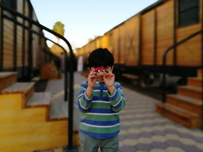 Boy holding toy car amidst freight trains