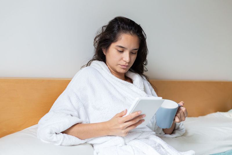 Young woman using mobile phone while lying on bed at home