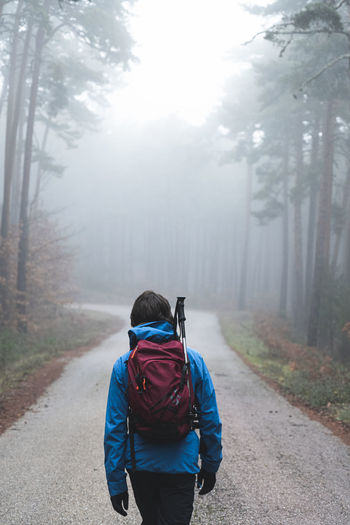 Male backpacker hiking along asphalt road cutting through foggy autumn forest
