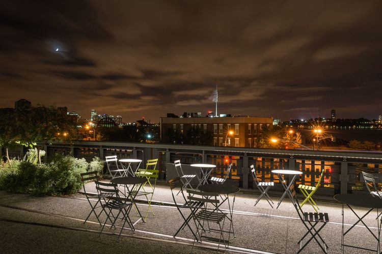 Chairs and tables on terrace against sky in city at night