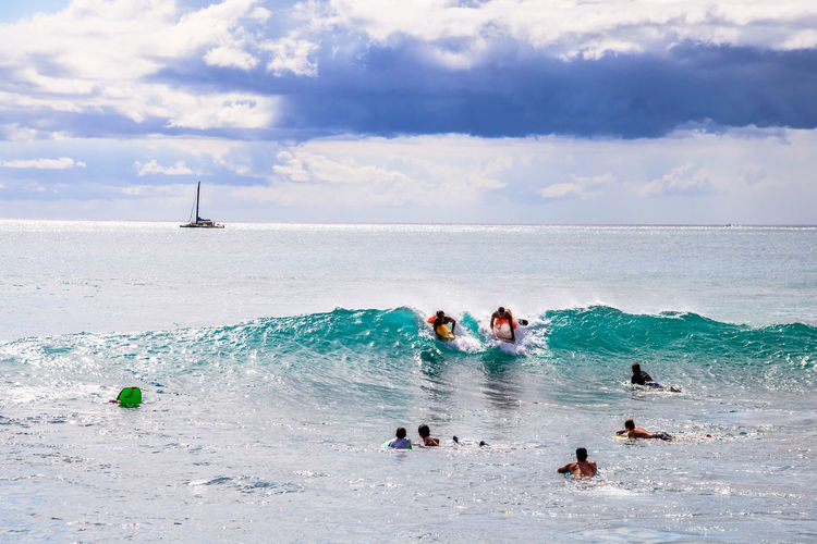 People surfboarding in sea against sky