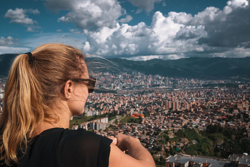 Woman looking at city buildings against cloudy sky