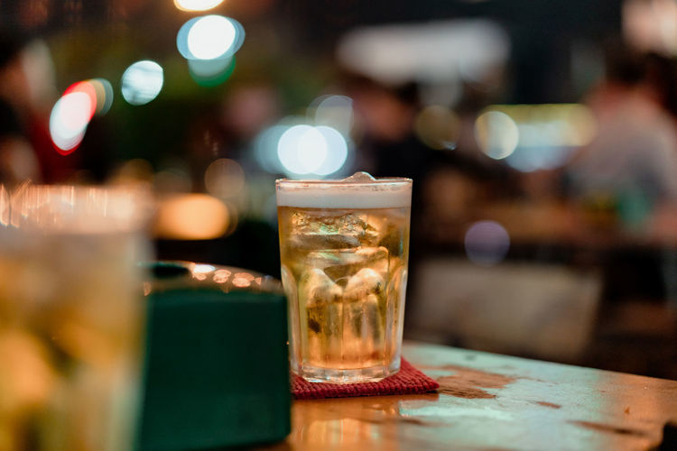 Image of a glass of beer on a wooden table in a tavern at night.