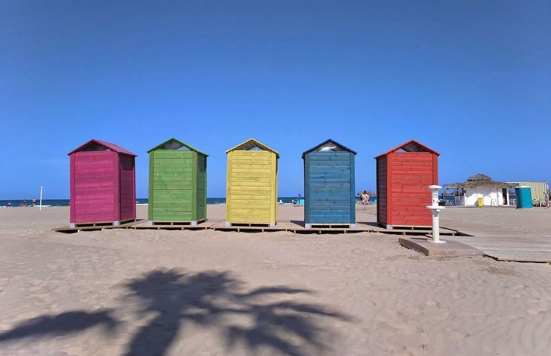 Beach huts against buildings against clear blue sky