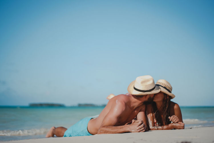 Couple embracing while lying down on sand at beach