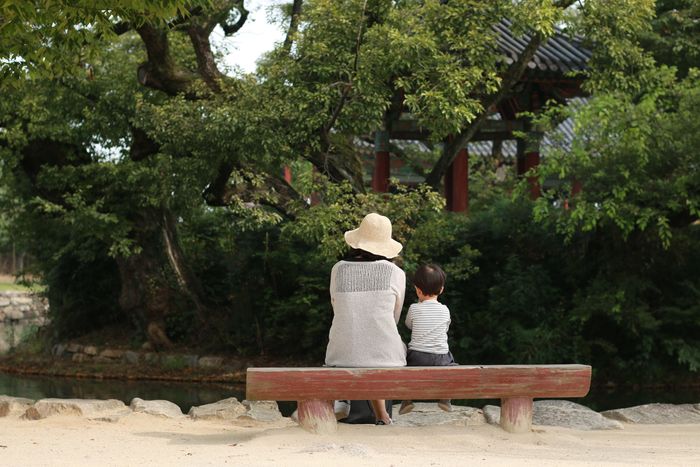 Rear view of mother and son sitting on bench at park