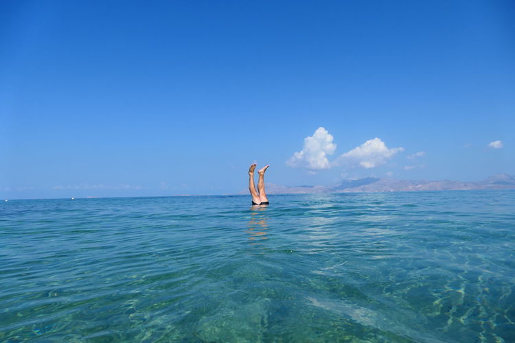 Man swimming in sea against clear blue sky in handstand