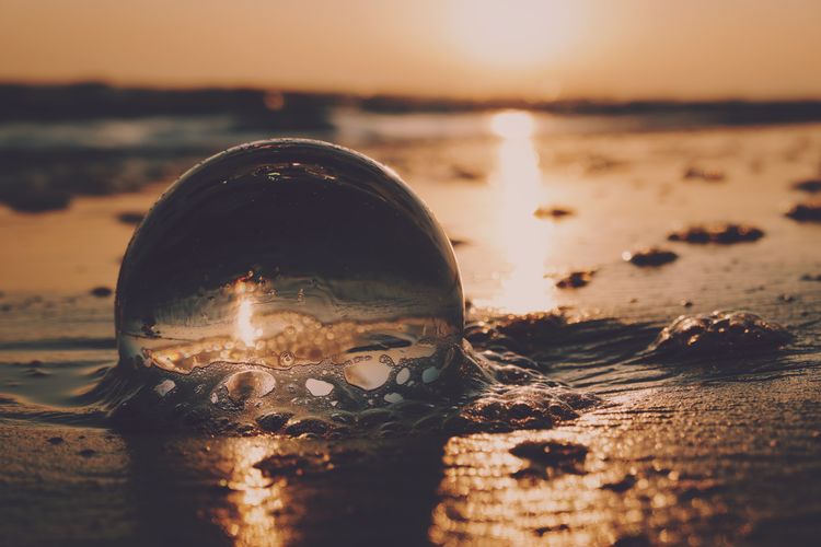 Close-up of crystal ball on beach against sunset sky