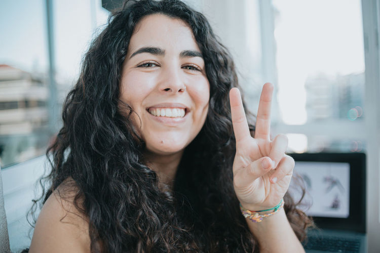Close-up portrait of smiling young woman gesturing peace sign