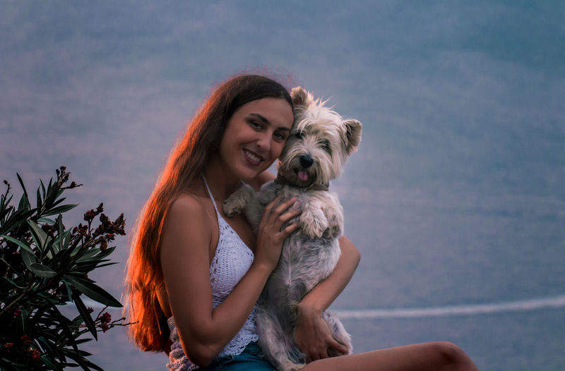 Portrait of young woman with dog against sky