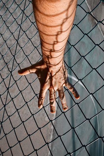 Hand with shadow shapes grabbing a metallic fence