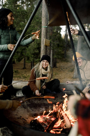 Happy male and friends enjoying food at campfire in forest