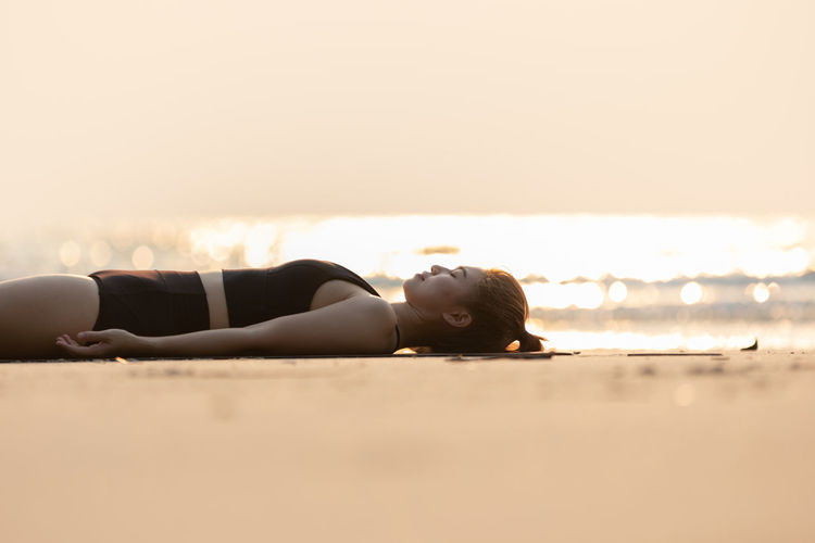 Young woman resting at beach against sky during sunset