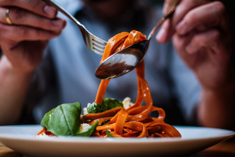 Close-up of person eating spaghetti with fork and spoon