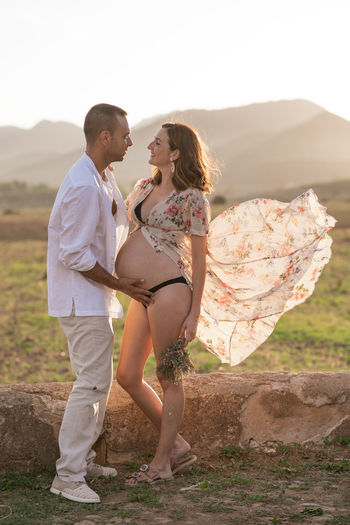 Pregnant woman standing with man against sky