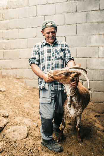 Smiling male goat herder standing with goat in front of wall