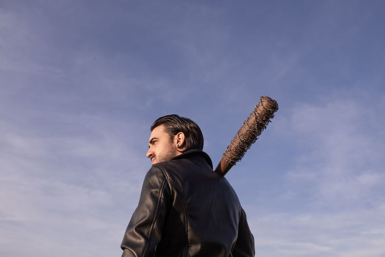 Mid adult man with barbed wire wrapped baseball bat looking away against sky