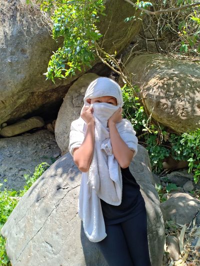 Portrait of woman covering face with scarf while standing by rock