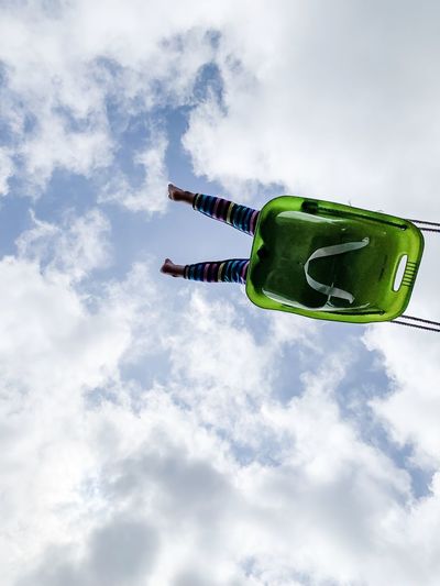 Low angle view of girl in swing against cloudy sky