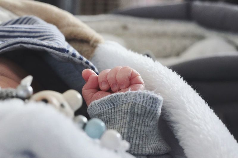 Cropped image of baby lying on bed at home
