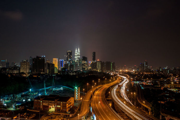 Illuminated modern buildings in city against sky at night