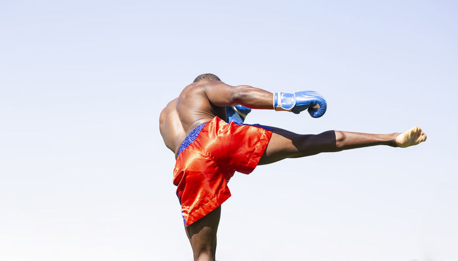 Active male athlete doing boxing exercise against clear sky on sunny day
