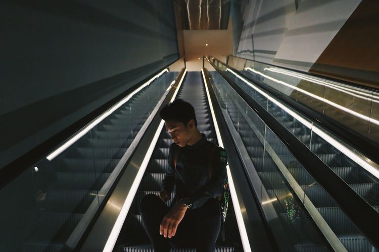 Young man sitting on escalator