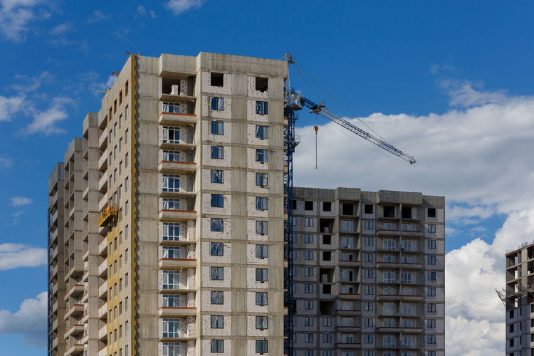 Building process of large residential apartment building with crane on cloudy sky background