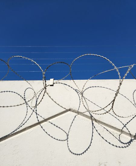 Barbed wire on white wall and blue sky. abstractnaf photo with symmetry and shadows